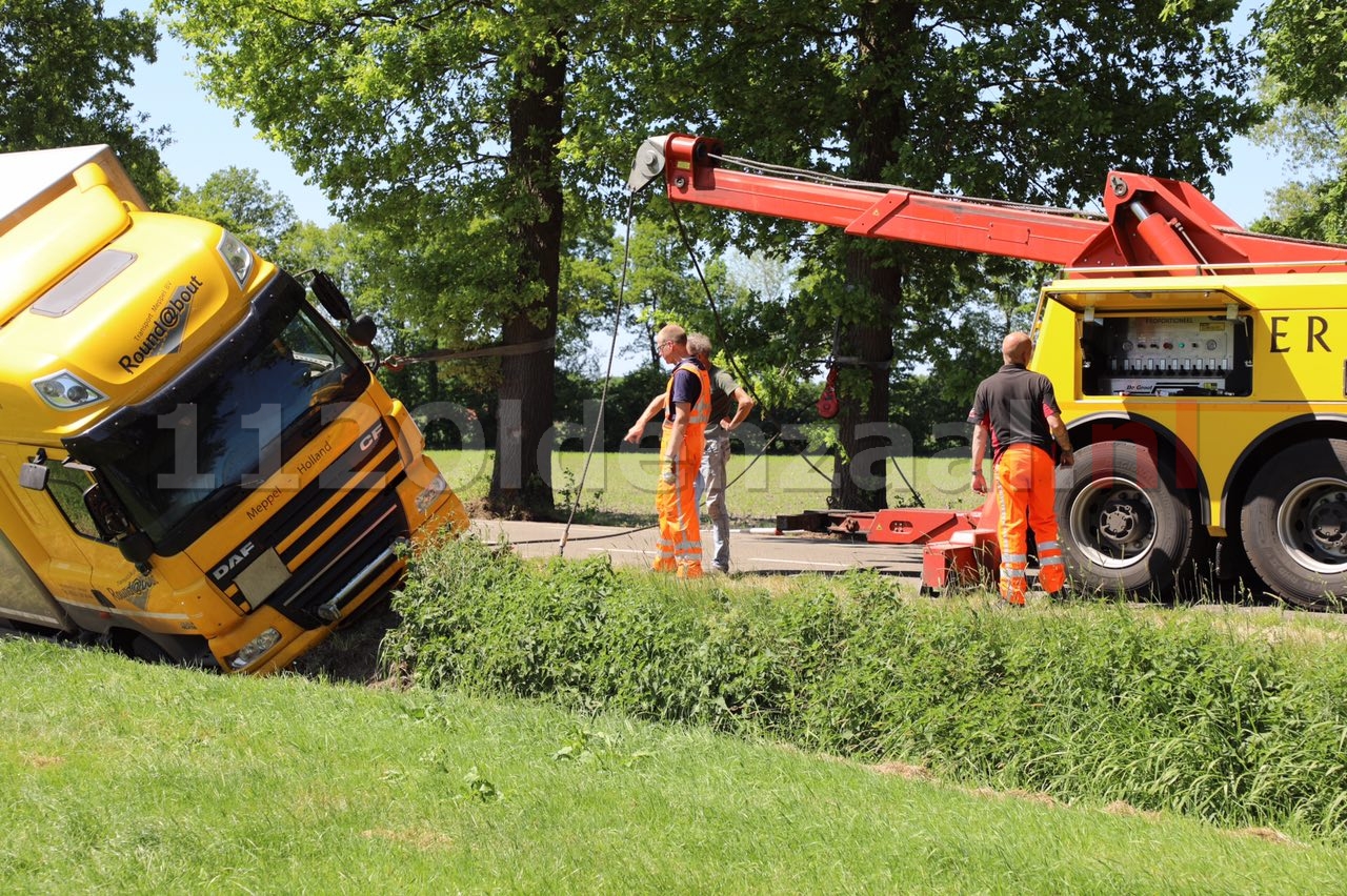 Vrachtwagen op zijn zijkant in sloot Saasveld